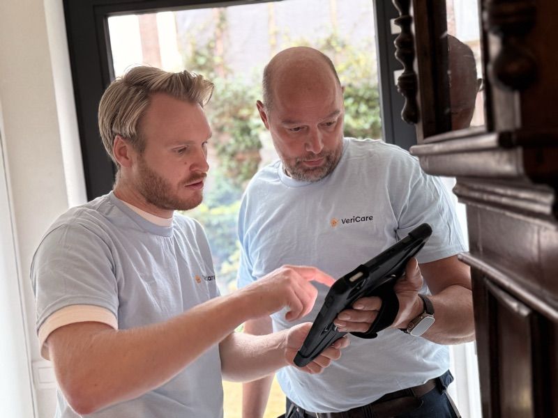 Twee VeriCare-medewerkers bekijken samen een woningrapport op een tablet in de inkomhal van een woning.